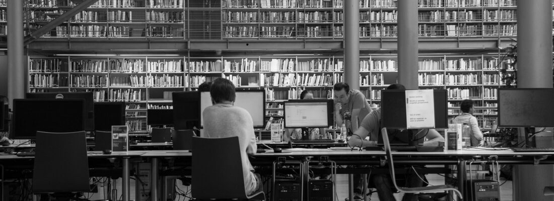 A black and white photo of people working at computers in a library.